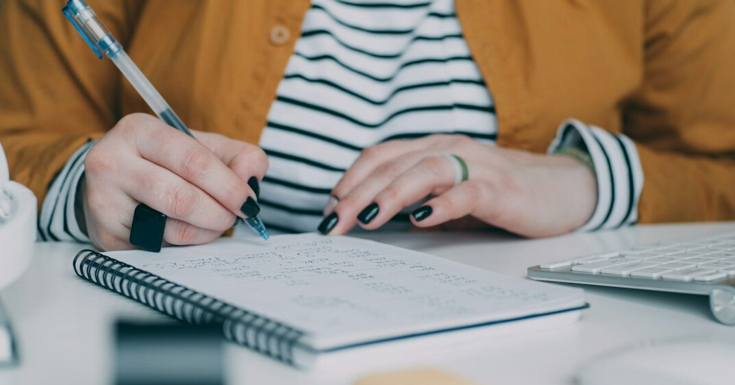 person writing expenses in notebook